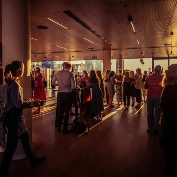 An indoor event in the evening, people wearing business clothes talking