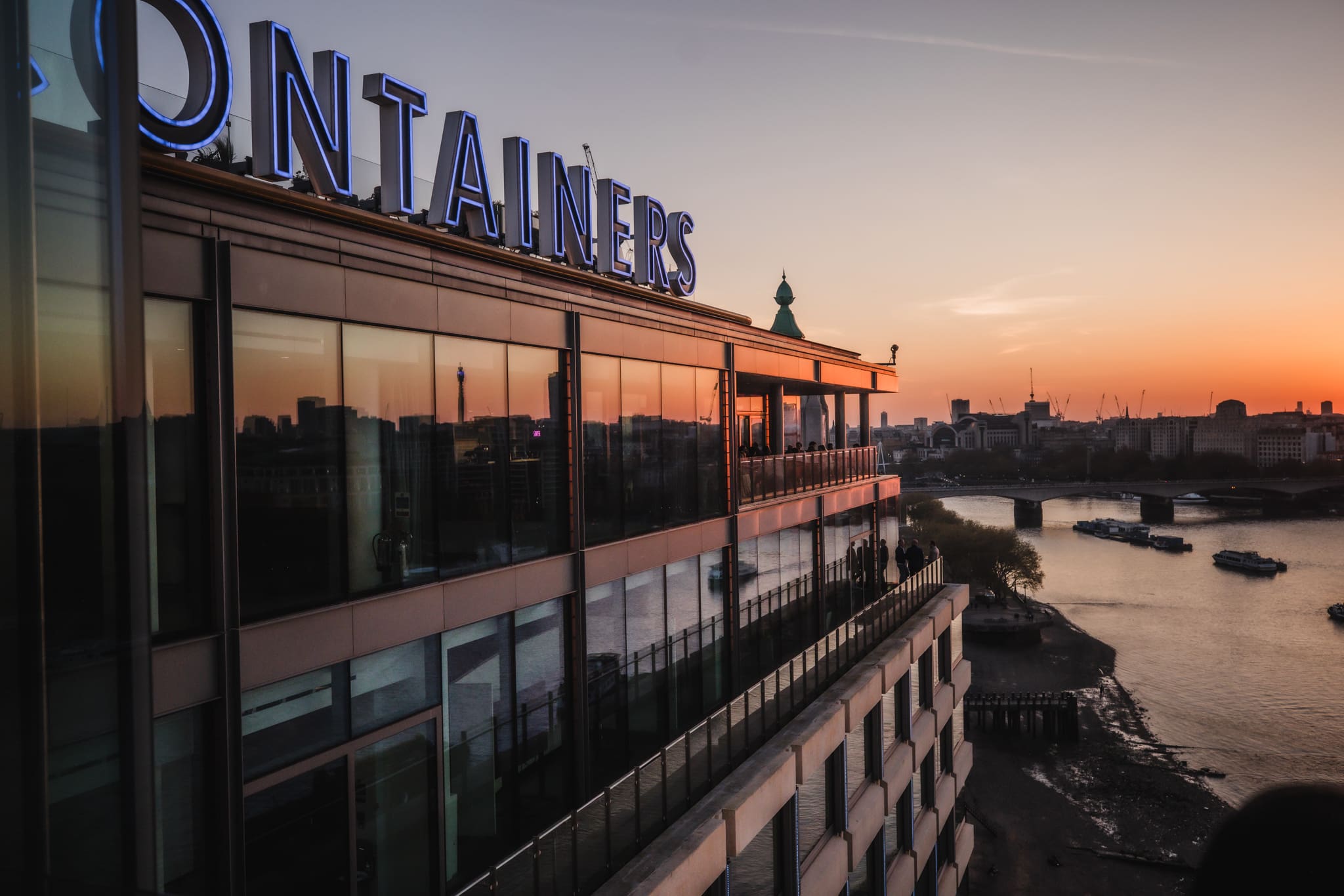 A modern riverside building at sunset with large blue letters spelling 